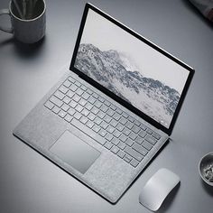 an open laptop computer sitting on top of a desk next to a mouse and coffee cup