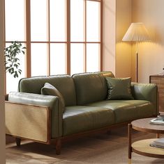 a green leather couch sitting in front of a window next to a table with a lamp on it