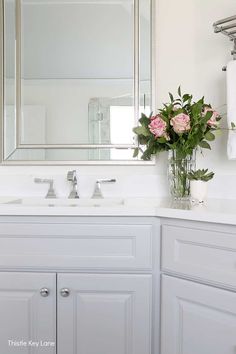 a bathroom with white cabinets and pink flowers in the vase on the sink countertop