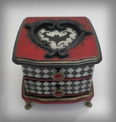 an ornate red and black box with a heart on the top is sitting on a white surface