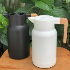 two plastic jugs sitting next to each other on top of a wooden table in front of green plants