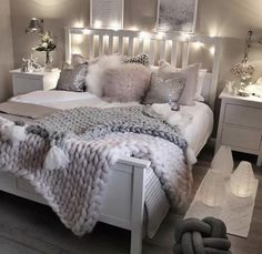 a white bed topped with lots of pillows next to two night stands and lights on the wall