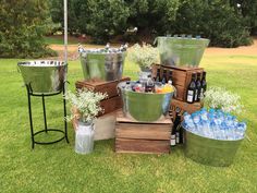 several metal buckets filled with bottles and water on top of grass next to trees