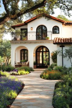 a white house with lots of plants and flowers around it's front porch area