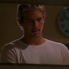 a man in a white shirt looking at the camera with a clock on the wall behind him