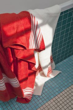 red and white towels hanging on the side of a bath tub next to tiled walls