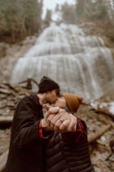 a man and woman standing in front of a waterfall pointing their fingers at the camera