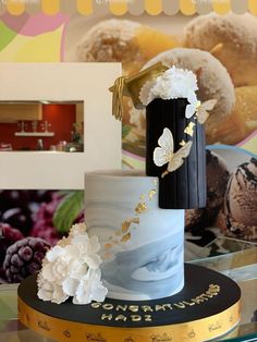 a three tiered cake with white flowers and gold decorations on top, sitting on a table