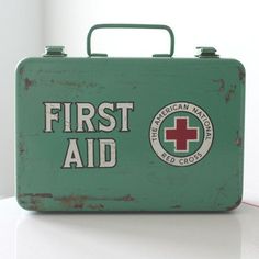 an old green first aid kit sitting on top of a white table next to a red cross sign