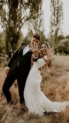 a bride and groom posing for a photo in the grass with their hands up to them