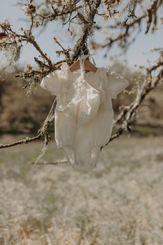 a white dress hanging from a tree branch in the middle of a dry grass field