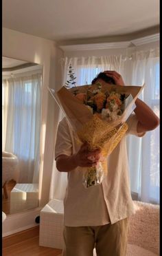 a man holding flowers in front of his face while standing next to a large mirror