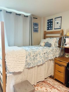 a bed sitting next to a window in a bedroom under a white blanket on top of a wooden headboard