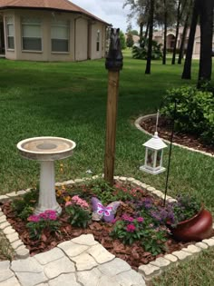 a bird bath sitting in the middle of a flower bed next to a lamp post