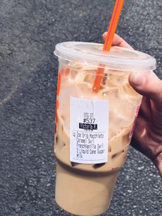 a person holding up a plastic cup filled with coffee and ice cream on the street