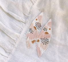 a pair of pink and white beaded earrings on top of a piece of cloth