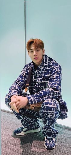 a young man sitting on the ground with his hands in his pockets, wearing blue and white patterned pajamas