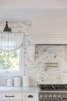 a white kitchen with marble backsplash and stainless steel stove top oven, window over the sink