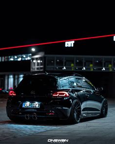 the back end of a black car parked in front of a building with red lights