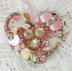 a heart shaped brooch sitting on top of a white lace covered table next to a pink ribbon