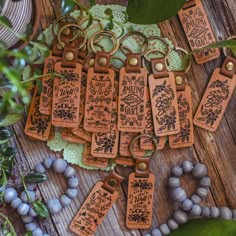 several leather tags with words and flowers on them sitting next to some beads, plants and leaves