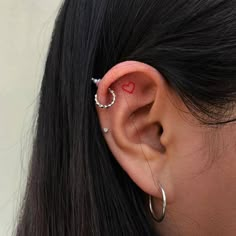 a woman's ear has a small red heart on it and is attached to the side of her ear