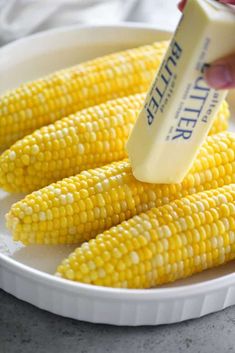 corn on the cob with butter being drizzled over it and sitting on a white plate