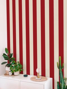 a room with red and white striped wallpaper, potted plants on top of a dresser