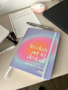 a notebook sitting on top of a desk next to a pen and laptop computer with the words it's okay to do it all