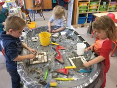 three children are playing with sand and tools