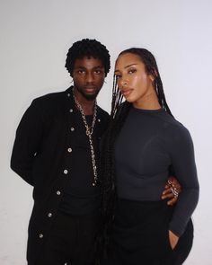 two people standing next to each other in front of a white wall and one is wearing a black shirt