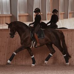 a woman riding on the back of a brown horse next to a wooden wall in an arena