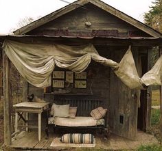 an outhouse with a couch and table in the front yard, covered by drapes