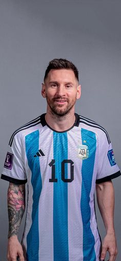 a man with tattoos standing in front of a gray background wearing a blue and white shirt