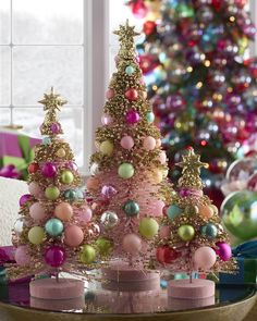 three pink christmas trees with gold stars and ornaments on them, in front of a brightly lit christmas tree