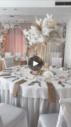 a table set up for a wedding with white flowers and gold place settings on it