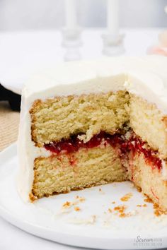 a cake with white frosting and strawberry jam on top is cut in half to show the inside