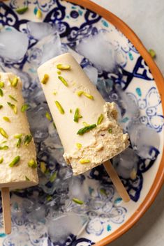 two ice pops with pistachio on them in a blue and white plate topped with ice