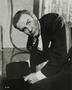 an old black and white photo of a man in a suit leaning on a chair