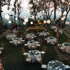 tables and chairs are set up outside for an outdoor party with paper lanterns hanging from the trees