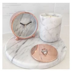 a marble table with a rose gold plate and candle holder on it, next to a marble clock