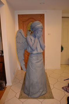 a statue of an angel with her hands to her face, standing in front of a door