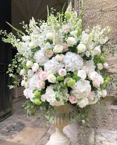 a vase filled with white and pink flowers sitting on top of a stone floor next to a doorway