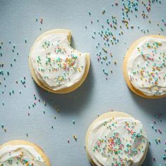 four cookies with white frosting and sprinkles on a blue tablecloth