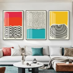 three abstract paintings hang on the wall above a white couch and coffee table in a modern living room