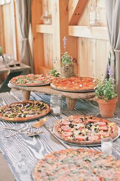 a table topped with lots of pizzas on top of wooden tables next to potted plants