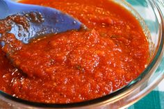 a spoon full of marinara sauce in a glass bowl with a blue and white checkered table cloth