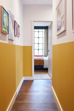 the hallway is painted yellow and white with pictures on the wall above it, along with an empty bed