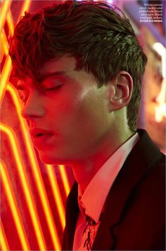 a young man wearing a suit and tie in front of neon lights with his eyes closed