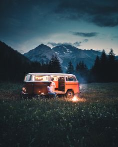 two people sitting in the back of an old van at night with mountains and trees behind them